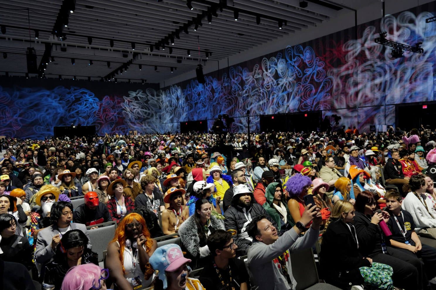 A packed panel hall at New York Comic Con, the audience in cosplay with the show's artwork projected across the back wall